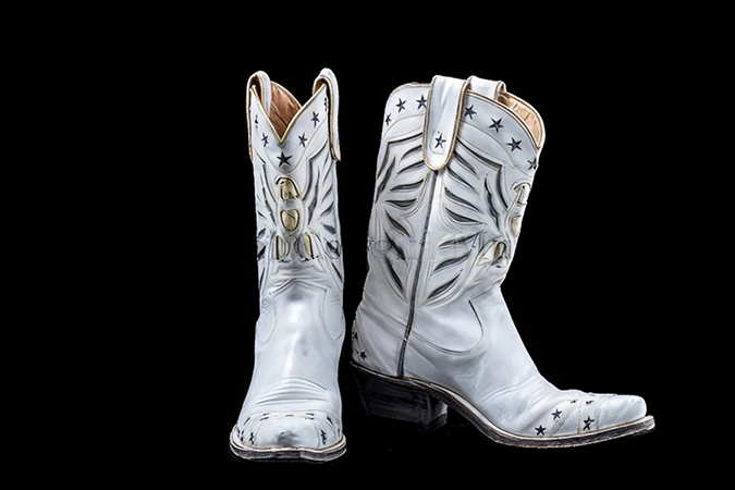 A pair of silver cowboy boots with black star decorations and metal accents shown against a black background.