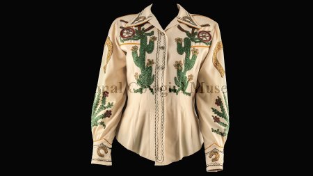 A cream-colored Western shirt featuring green cactus, brown horseshoe, and wagon wheel embroidery with decorative stitching on the front, sleeves, and cuffs.
