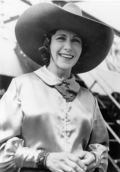 Smiling woman in a huge wide-brim hat and satin blouse, wearing vintage 1930s–40s fashion.
