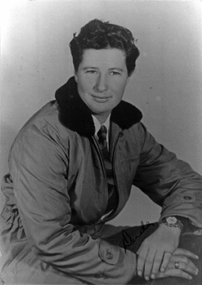 Black-and-white portrait of a man in a coat with a fur collar, seated and looking at the camera.