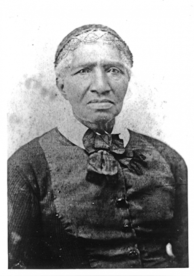 Historical black-and-white portrait of an older Black woman wearing a dark cardigan and a large bow at the neck, facing forward.
