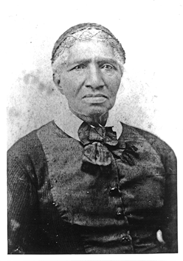 Historical black-and-white portrait of an older Black woman wearing a dark cardigan and a large bow at the neck, facing forward.