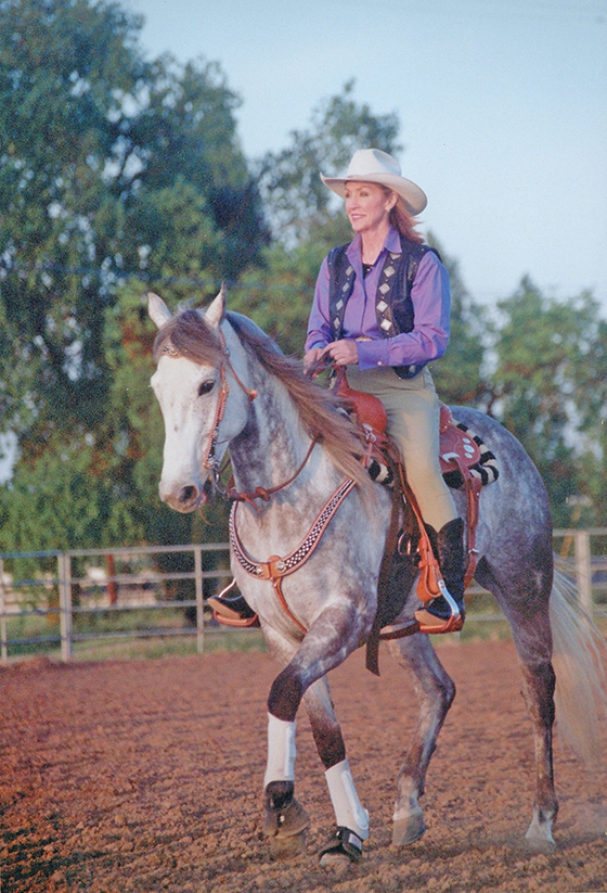 Woman in a white cowboy hat rides a gray horse in an outdoor arena.