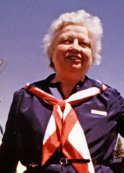 Smiling elderly woman with short white hair wearing a navy shirt and a red-and-white scarf outdoors.