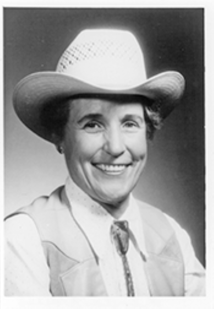 Smiling woman in a white cowboy hat and western shirt, facing the camera.