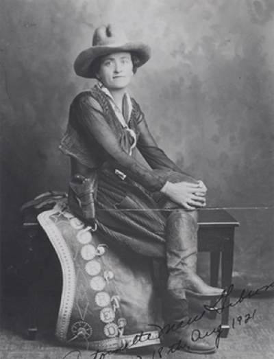 Historic portrait of a young woman in a long dress and wide-brim hat, seated on a bench, with a handwritten inscription dated Aug 1921.