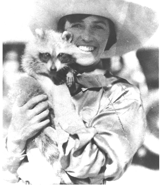 Smiling woman in a wide-brimmed hat holding a fluffy cat outdoors.