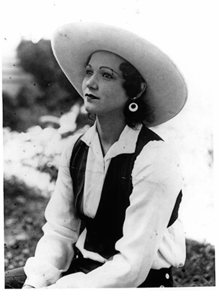 Black-and-white portrait of a woman in a wide-brimmed hat, white blouse, and dark vest, outdoors.