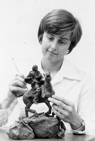 Female sculptor chiseling a horse statue, using a hammer and chisel in a studio.