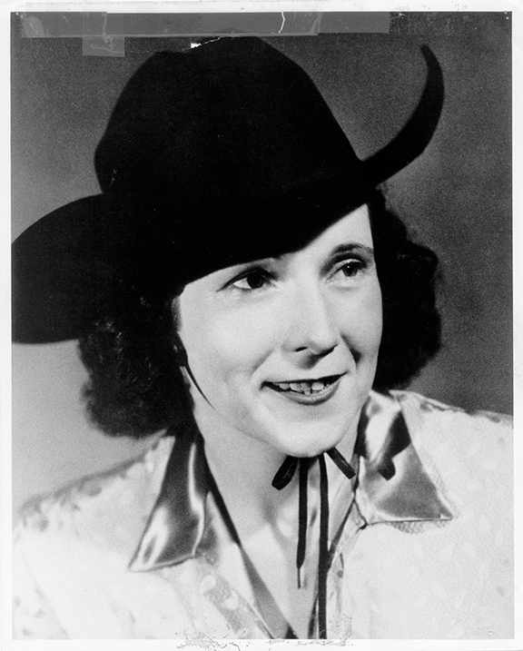 Black-and-white portrait of a smiling woman wearing a wide-brim hat and satin blouse with a ribbon tie.