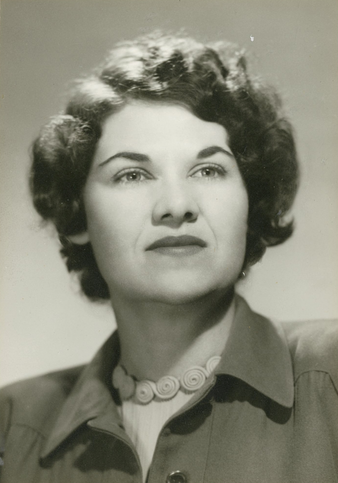 Close-up black-and-white portrait of a woman looking upward, with short, wavy hair and a beaded necklace.
