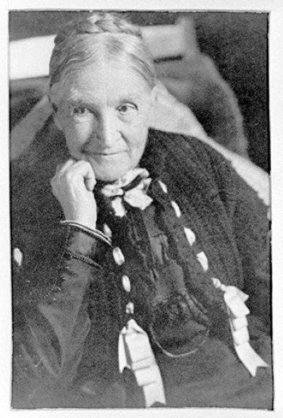 Portrait of an elderly woman in a dark dress with ribbons, resting her chin on her hand.