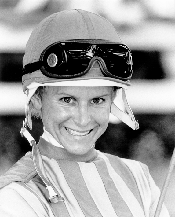Smiling female jockey wearing a helmet and goggles, striped racing silks, preparing for a race