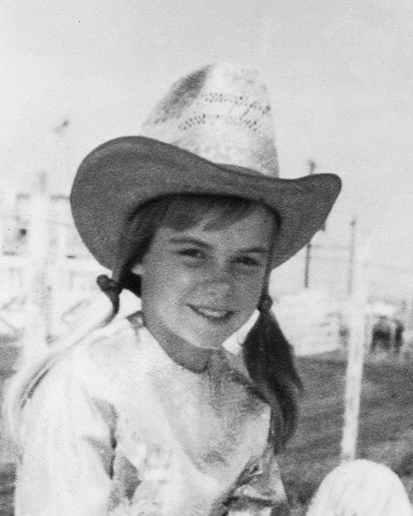 Young girl wearing a straw cowboy hat and braided pigtails, smiling outdoors in a vintage photo