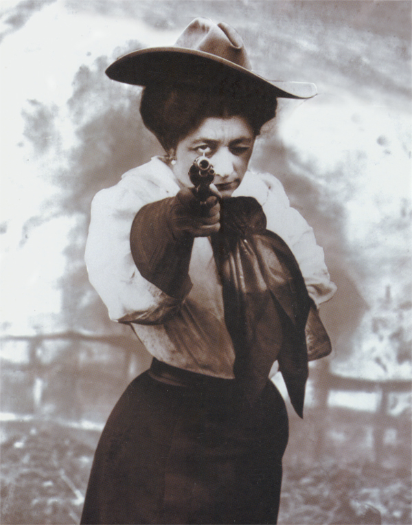 Woman in a vintage outfit wearing a wide-brimmed hat points a pistol directly at the camera, aiming with intent.