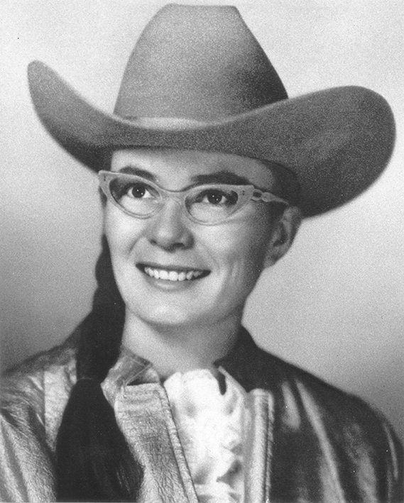 Smiling woman wearing a cowboy hat and glasses, with braided hair, in a western-style outfit.