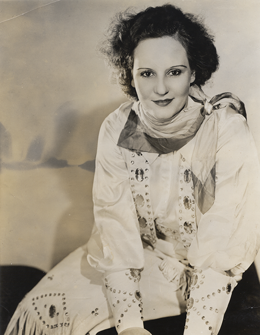 Black-and-white portrait of a woman in a rhinestone-studded white stage costume with a scarf, looking at the camera.