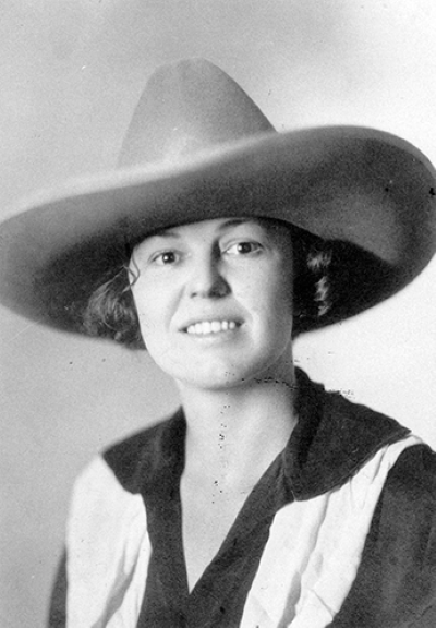 Black-and-white portrait of a smiling woman wearing a wide-brimmed hat and a v-neck blouse, capturing a vintage style.