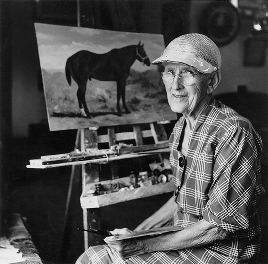 Older woman in a plaid dress sits in her studio, painting a horse on a canvas propped on an easel, with a painter's palette nearby.