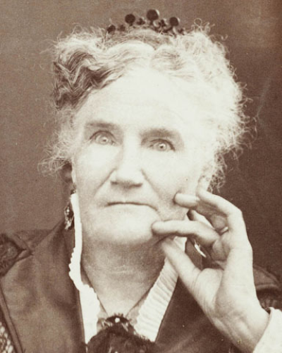 Portrait of an elderly woman with light hair, wearing a small crown and a dark dress, resting her chin on her hand.