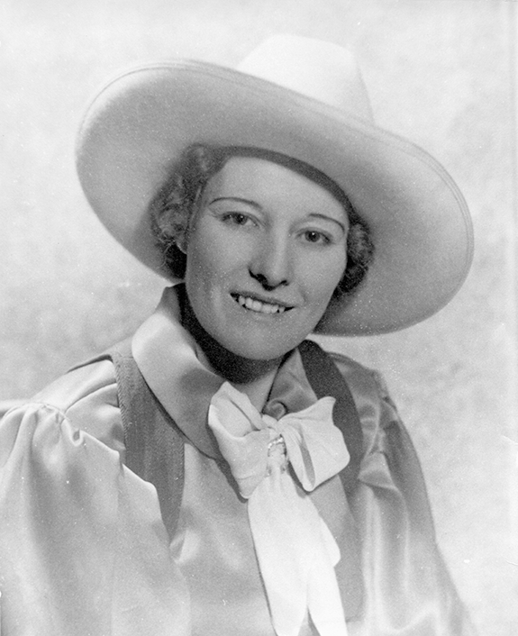 Portrait of a smiling woman wearing a large wide-brim hat, satin blouse, and a bow tie in a vintage studio portrait, 1920s style.