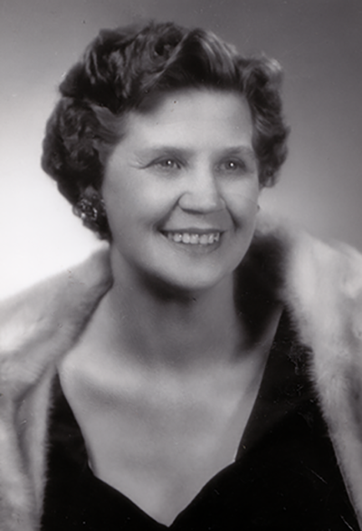 Smiling woman in a black dress with a fur stole, vintage portrait style.