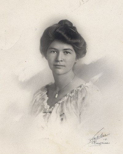 Vintage studio portrait of a young woman with short, styled hair wearing a light, ruffled blouse and a necklace.