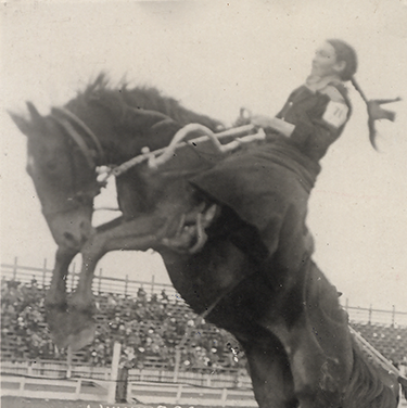 Portrait of Fannie Sperry-Steele riding a bucking horse at the Winnipeg Stampede, 1913; caption reads 'World's Champion Lady Bucking-Horse Rider.'