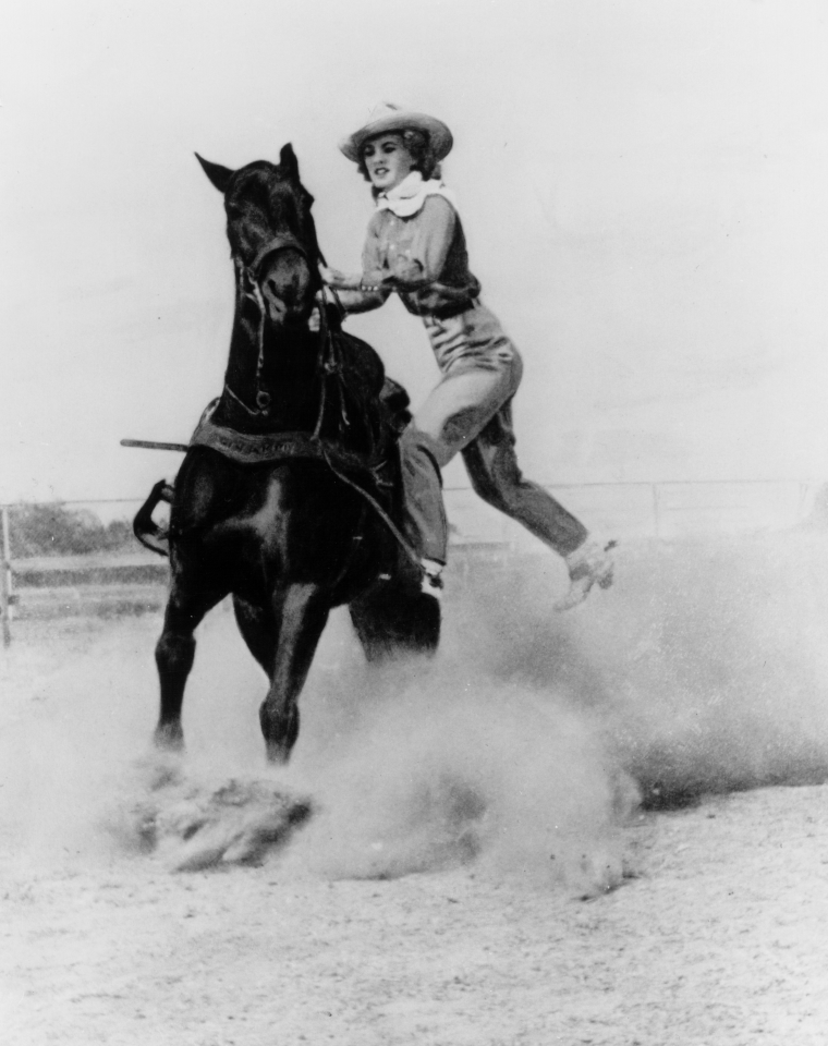 Person in a hat rides a horse that is rearing in a snowy field, black-and-white photo