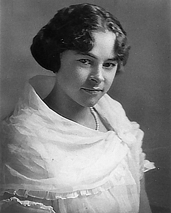 Vintage studio portrait of a young woman with short curled hair, wearing a white off-shoulder dress and a pearl necklace.