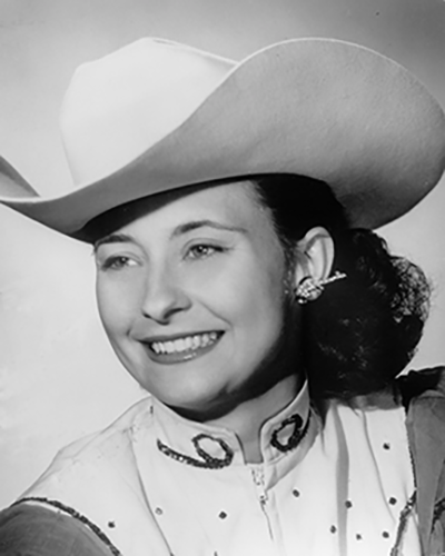 Black-and-white portrait of a smiling woman wearing a wide cowboy hat and a western-style blouse.