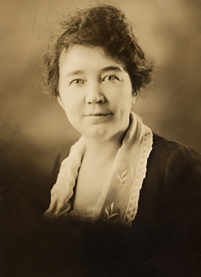 Sepia-toned studio portrait of a woman with short dark hair, wearing a light scarf and dark top, facing the camera.