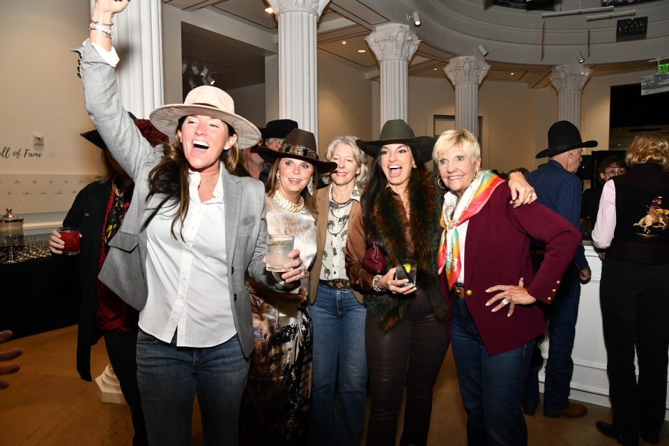 Group of adults at a party wearing wide-brim hats and smiling, holding drinks indoors.