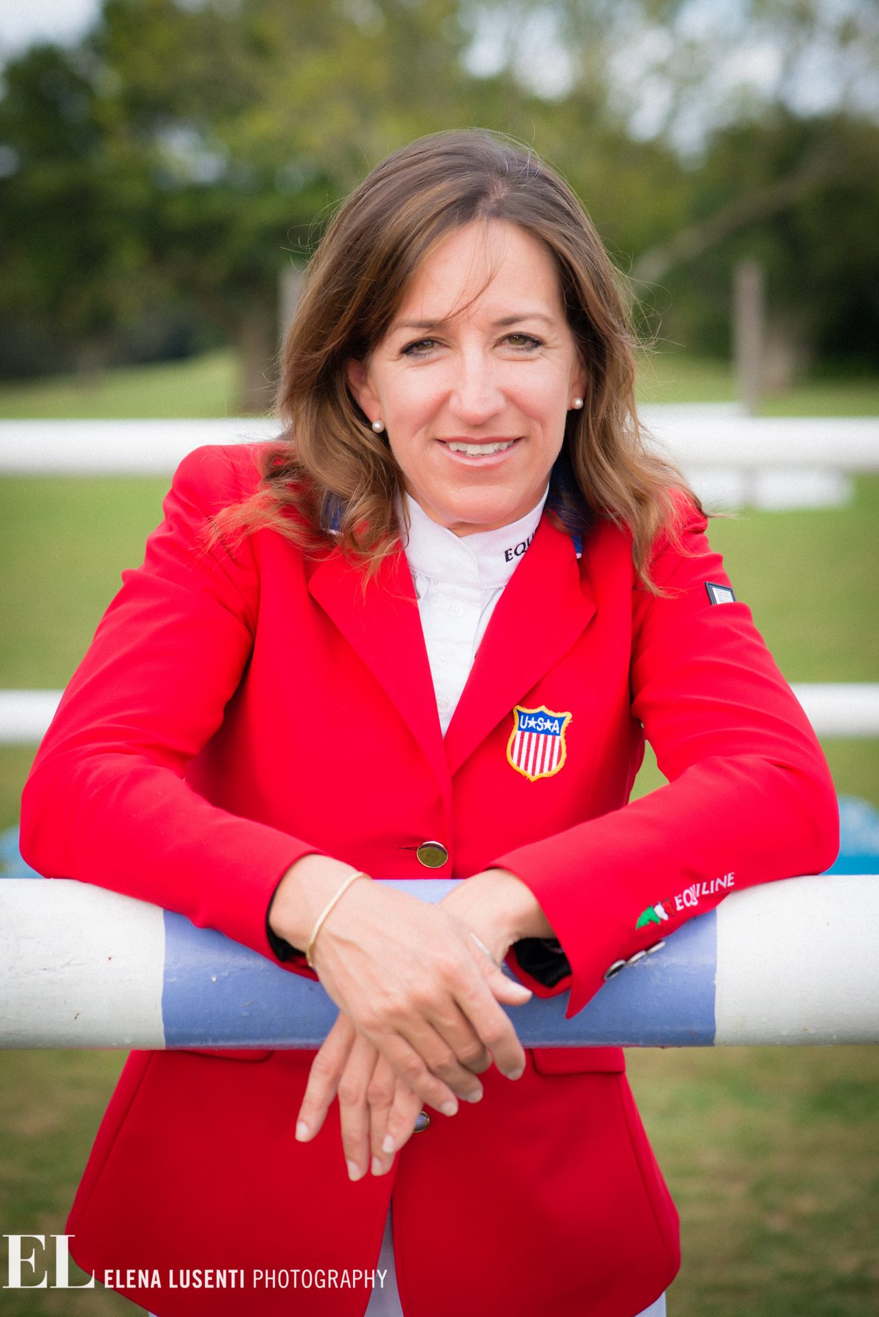 Portrait of a woman in a red blazer with a USSA crest, leaning on a white and blue railing outdoors.