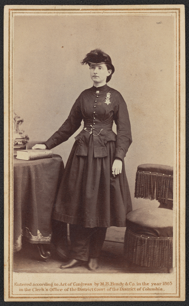 1860s woman in a dark military-style dress with a medal, standing beside a table; caption notes Brady & Co. 1865 from the ledger at the bottom.