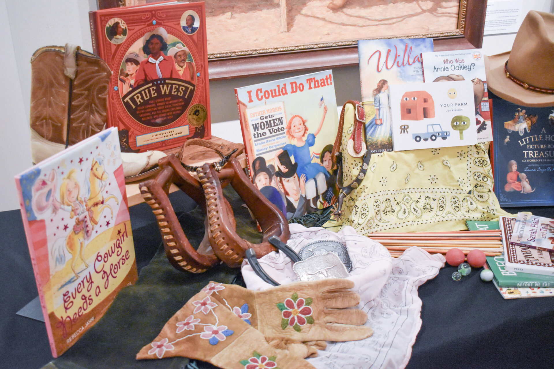 Display of vintage children's books, toys, and fabric items arranged on a shelf and table, including a large red 