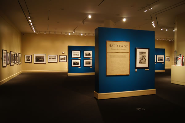 Interior of an art gallery with blue display walls showing framed photographs and a large text panel titled 'Hard Twist'