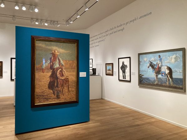 Large painting of a cowboy on horseback holding a lariat, mounted on a teal partition in an art gallery.